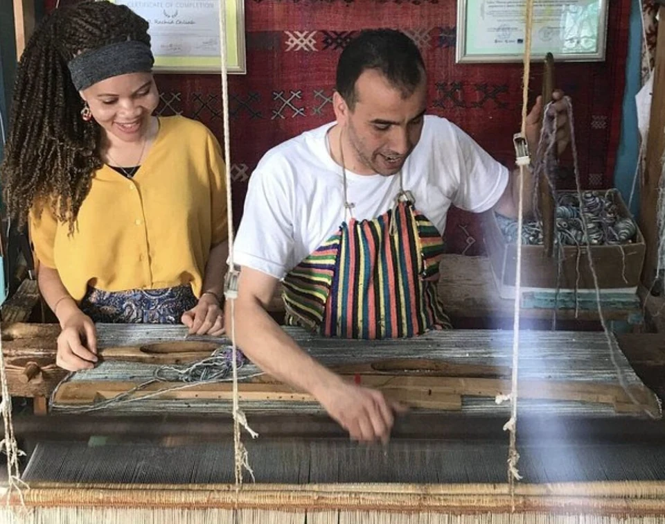 A smiling guest weaves her own row of a rug with Rachid in Chefchaouen
